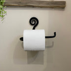 A black metal rustic toilet roll holder with a decorative spiral and a single hook arm, holding a white toilet paper roll against a beige wall.