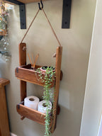Wooden hanging shelf with plants and toiletries on a neutral wall.