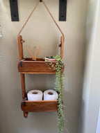 Wooden shelf with decorative elements and toilet paper rolls on a neutral wall.
