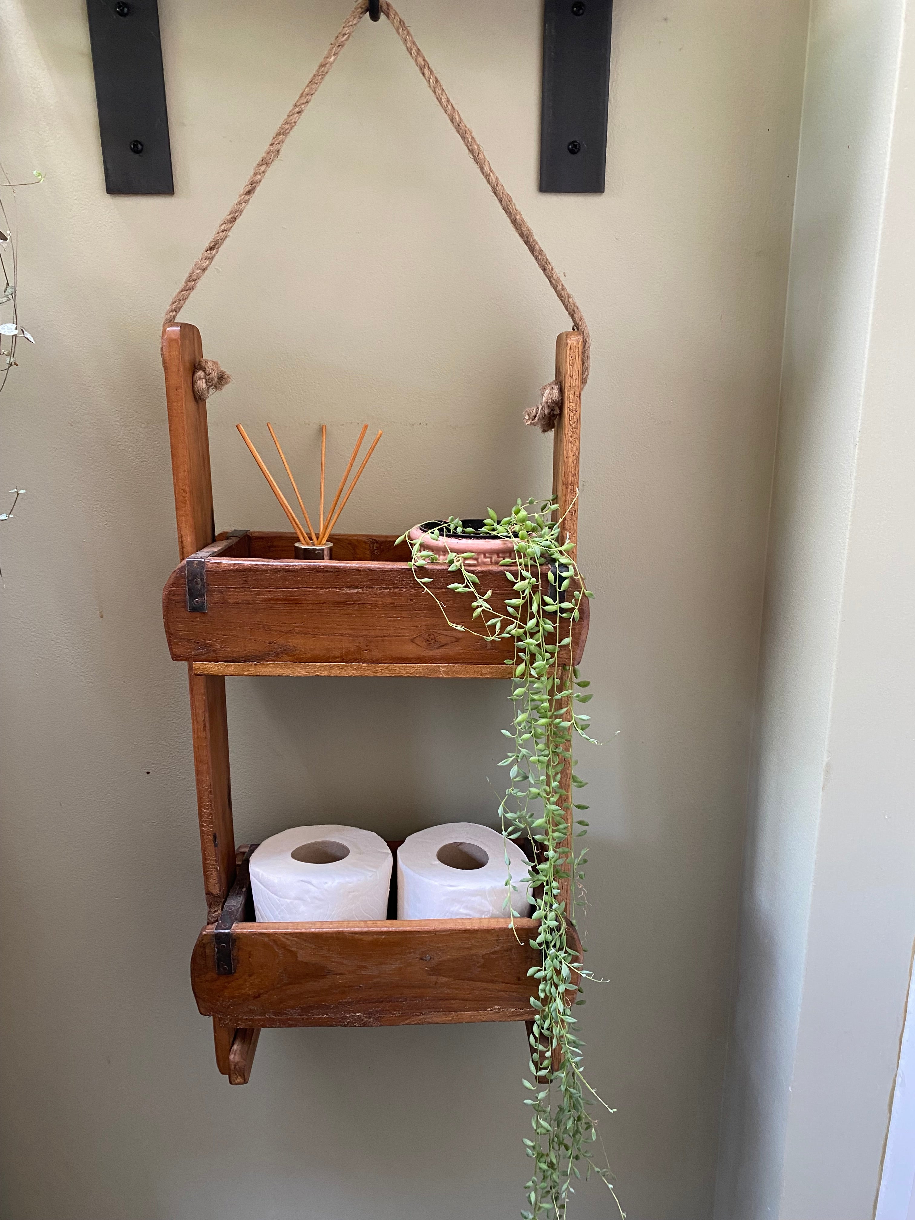 Wooden shelf with decorative elements and toilet paper rolls on a neutral wall.